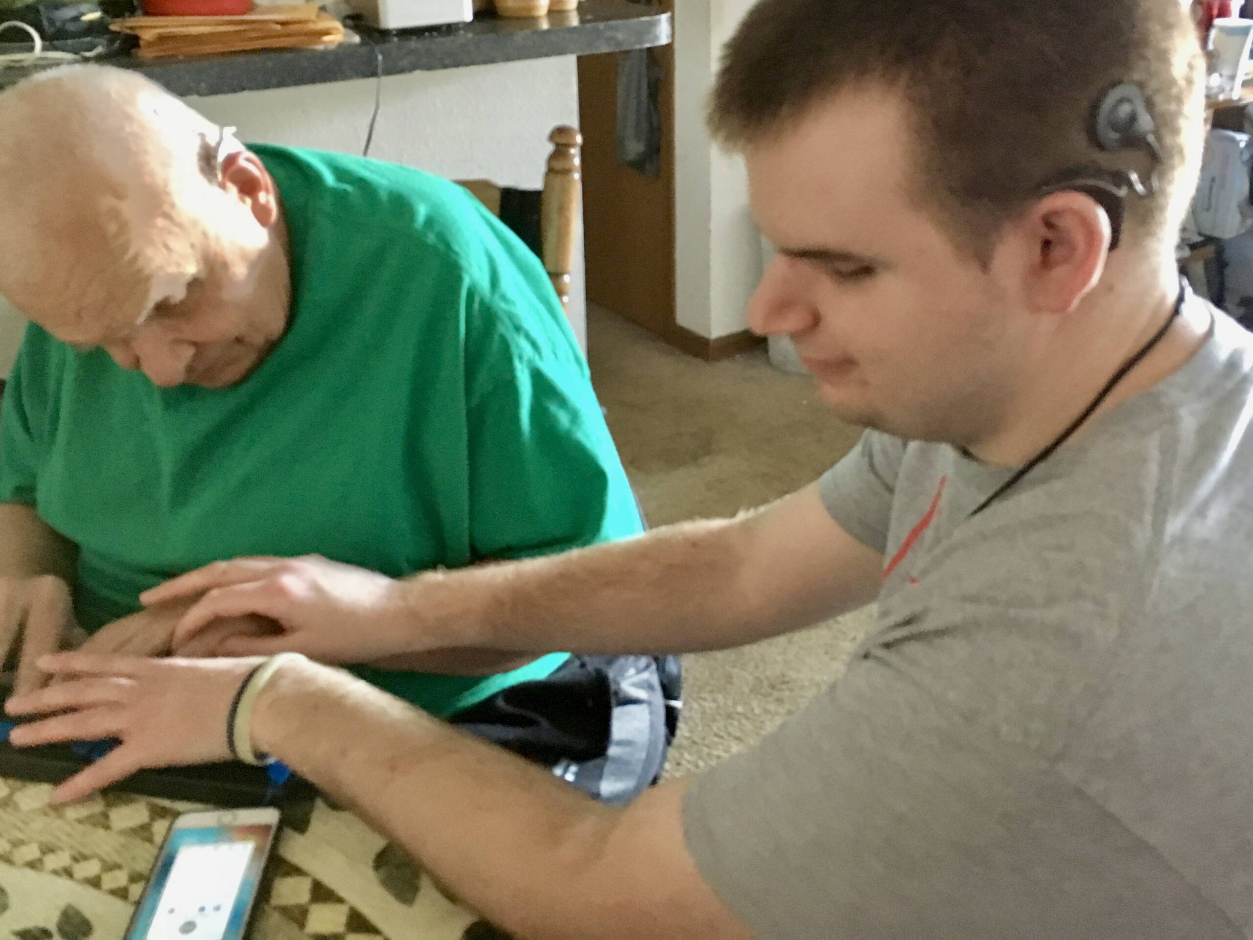 In the photo, Brett (on the right) is training iCanConnect Missouri consumer, Gary Jones, (left) on a braille device with his iPhone connected. Brett is using hand-over-hand training with Gary.