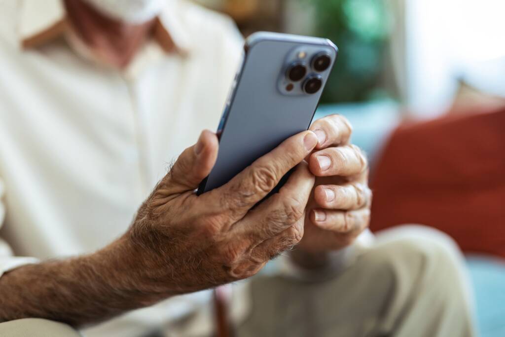 A close-up shot of an elderly man’s hands holding and using a blue smartphone.